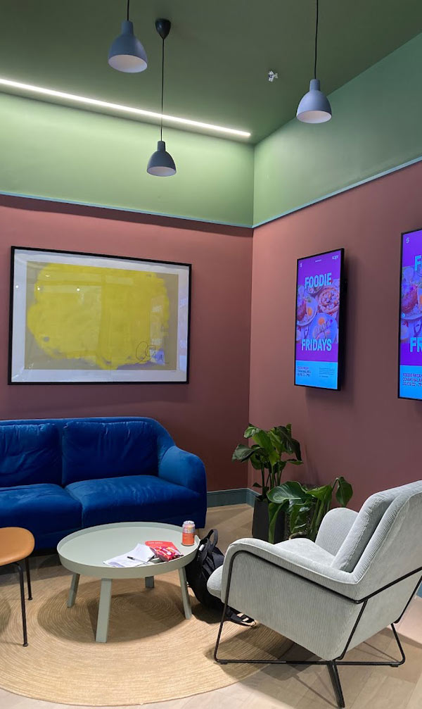 modern lounge area featuring a blue sofa, a light green coffee table, and a grey armchair surrounded by plants and artwork, ideal for dining and relaxation, highlighting vibrant wall colors