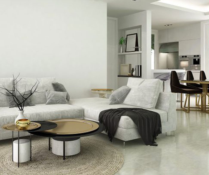 Modern living room with a light gray sectional sofa, a round coffee table featuring black and gold elements, and a textured circular rug; natural light fills the space from an adjoining kitchen, creating an inviting and stylish atmosphere.