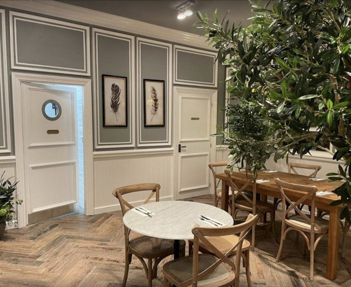 A modern and stylish restaurant interior featuring a marble table, wooden chairs, decorative plant, and framed artwork on the walls.