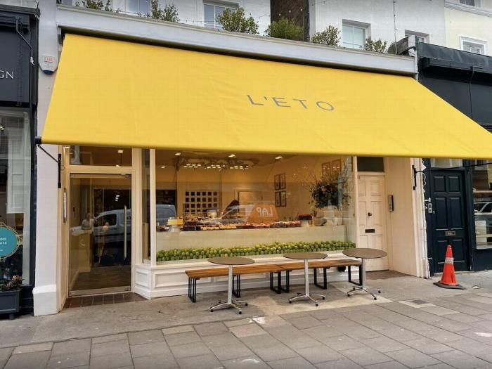 Yellow awning of L'Éto café with a window display showcasing pastries and green apples, featuring outdoor seating and modern entrance.